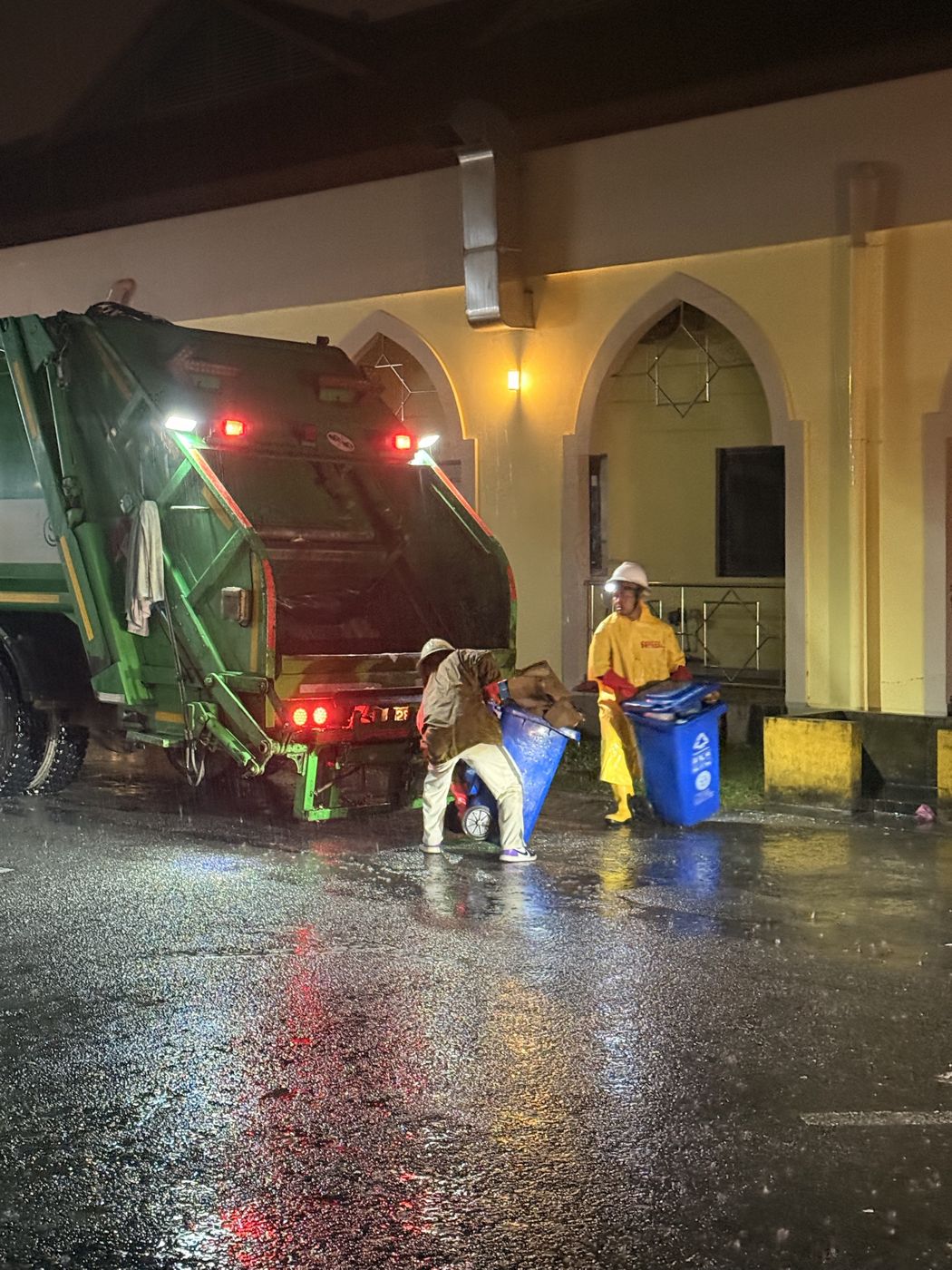 SHYT crew emptying bins into a compactor truck in the rain at night